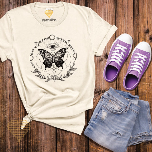 Ivory Comfort Colors tee with a black design of a butterfly, all-seeing eye, crescent moons, celestial symbols, and botanicals.