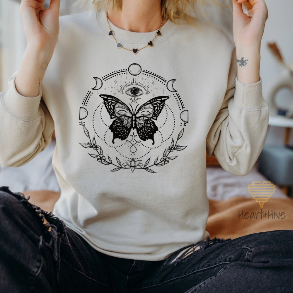 Sand crewneck sweatshirt with a black design of a butterfly, all-seeing eye, crescent moons, celestial symbols, and botanicals.