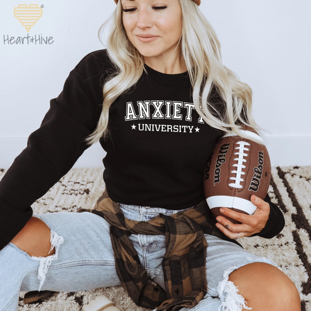 Black crewneck sweatshirt with 'Anxiety University' in bold, white collegiate font, framed by small stars.