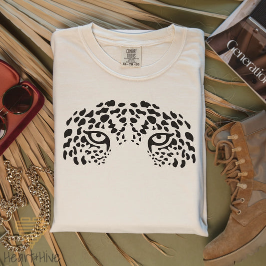 Ivory comfort colors tee with a face formed by bold black leopard spots, creating striking jaguar eyes that stare intensely.