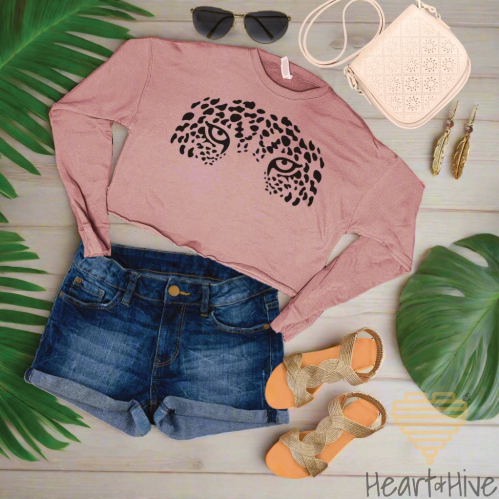 Mauve cropped fleece sweatshirt with a face formed by bold black leopard spots, creating striking jaguar eyes that stare intensely.