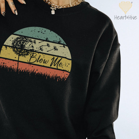 Black sweatshirt with a retro sunset circle, grass, and the faded silhouette of a dandelion and 'Blow Me' text.