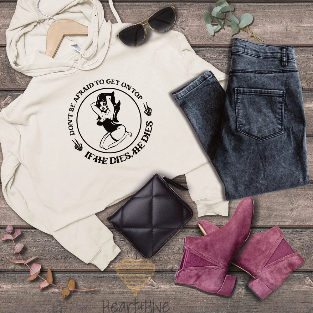 Heather dust crop hoodie with a circular design featuring a pin-up style woman, two skull hand peace signs, and the phrase 'Don't be afraid to get on top, if he dies, he dies.