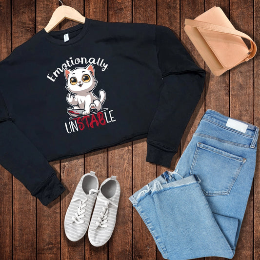 Black crop sweatshirt with a white cat holding a bloody knife with his middle finger up. 'Emotionally' is rounded above and unstable is written below with 'stab' red and dripping.