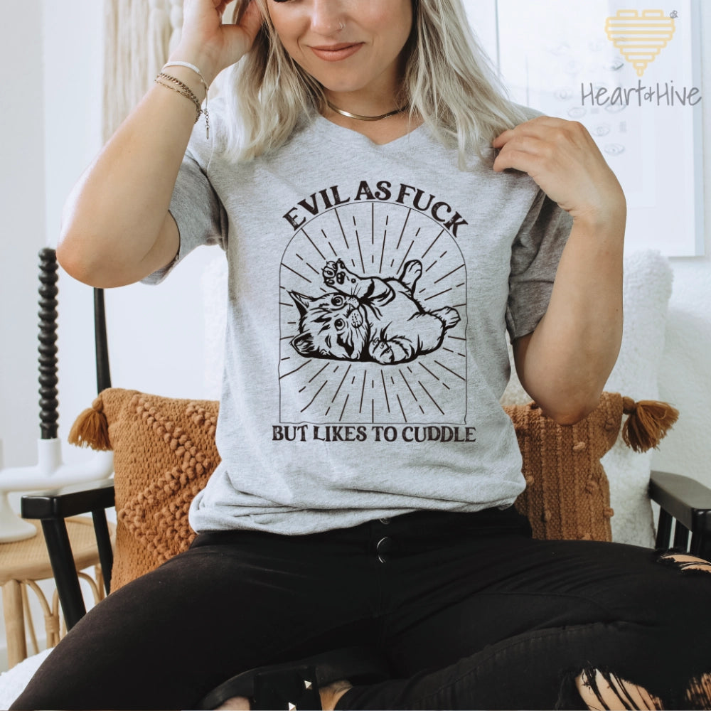 Athletic Heather Grey tee with a black line-art illustration of a kitten lying on its back inside a decorative arched frame with radiating lines. The text 'Evil as Fuck but Likes to Cuddle' is placed above and below the design.