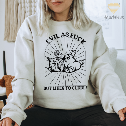 Sand sweatshirt with a black line-art illustration of a kitten lying on its back inside a decorative arched frame with radiating lines. The text 'Evil as Fuck but Likes to Cuddle' is placed above and below the design.