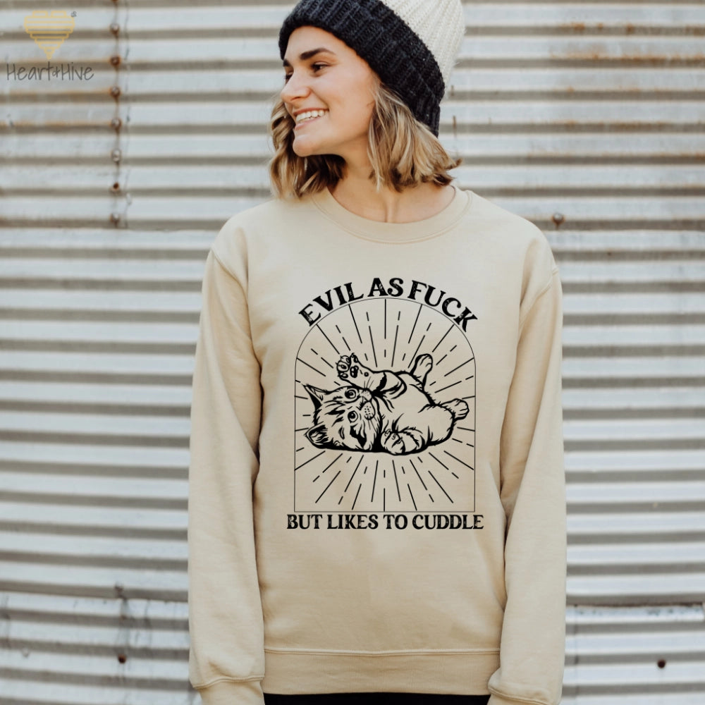 Sand sweatshirt with a black line-art illustration of a kitten lying on its back inside a decorative arched frame with radiating lines. The text 'Evil as Fuck but Likes to Cuddle' is placed above and below the design.