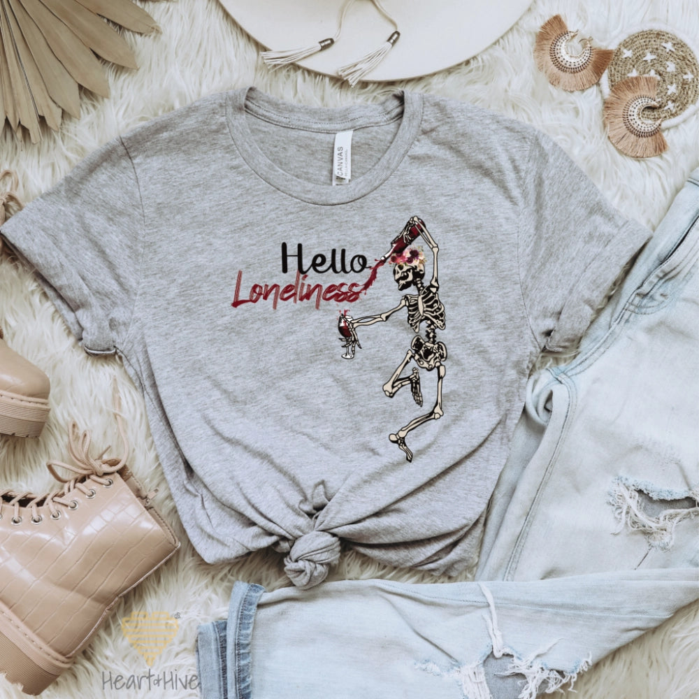Athletic heather grey tee with a leaping skeleton holding a bottle of wine, splattering red liquid across 'Hello Loneliness' in bold and script fonts.
