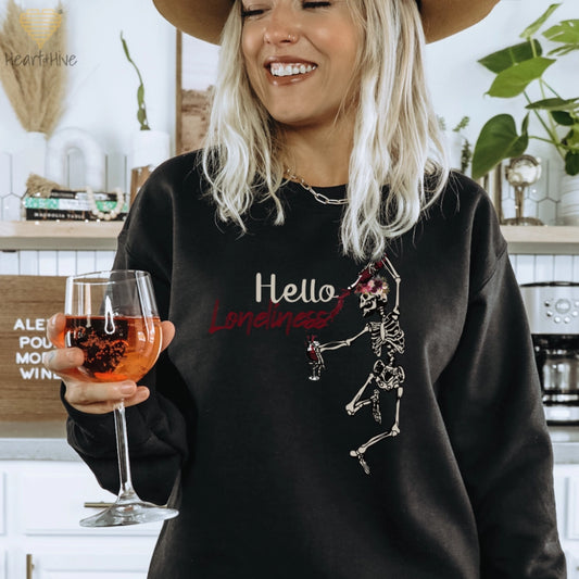 Black sweatshirt with a leaping skeleton holding a bottle of wine, splattering red liquid across 'Hello Loneliness' in bold and script fonts.
