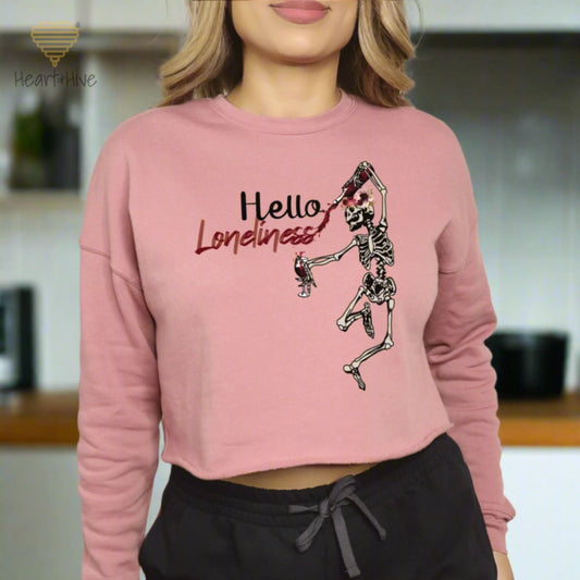 Mauve cropped crewneck fleece with a leaping skeleton holding a bottle of wine, splattering red liquid across 'Hello Loneliness' in bold and script fonts.