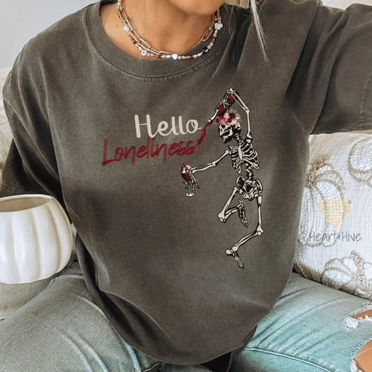 Pepper comfort colors tee with a leaping skeleton holding a bottle of wine, splattering red liquid across 'Hello Loneliness' in bold and script fonts.