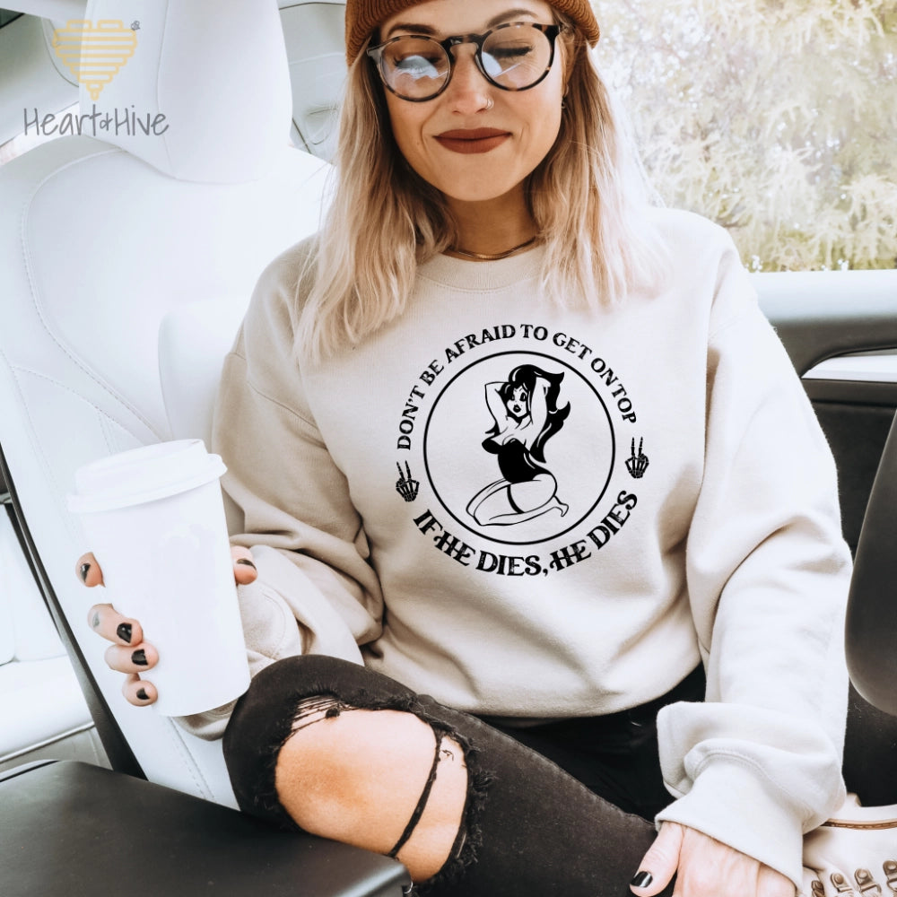 Sand sweatshirt with a circular design featuring a pin-up style woman, two skull hand peace signs, and the phrase 'Don't be afraid to get on top, if he dies, he dies.