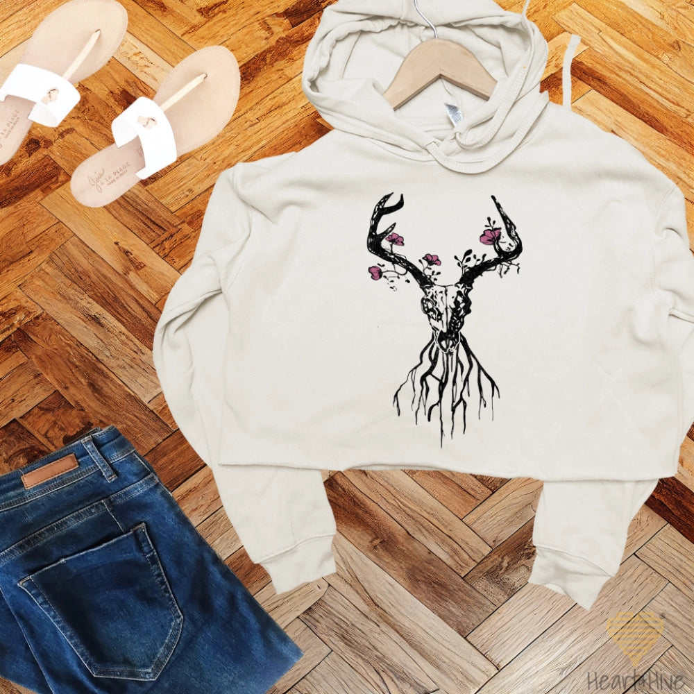 Heather dust crop hoodie featuring a deer skull with antlers, floral accents, and roots, blending rustic and boho aesthetics.