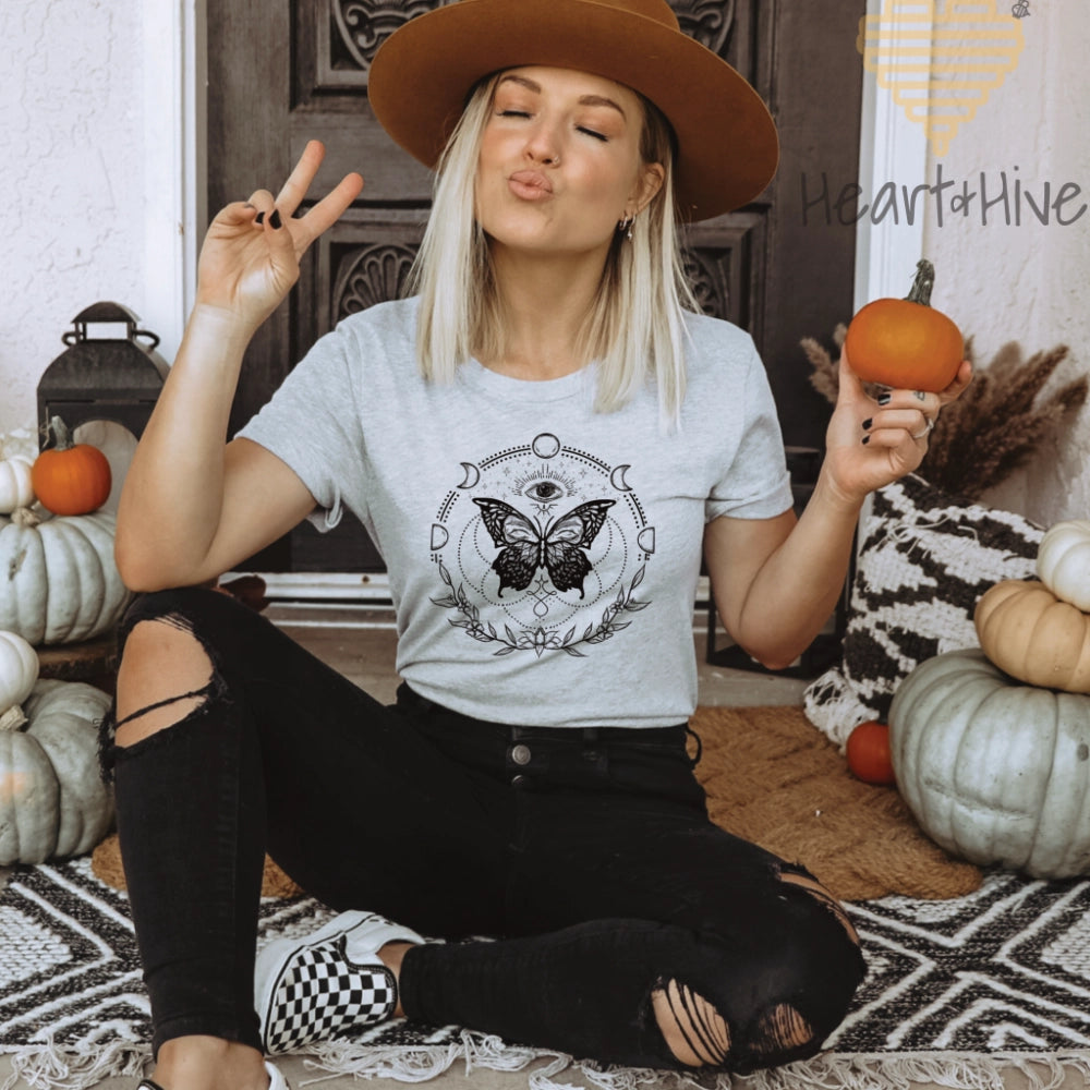 Athletic heather grey tee with a black design of a butterfly, all-seeing eye, crescent moons, celestial symbols, and botanicals.