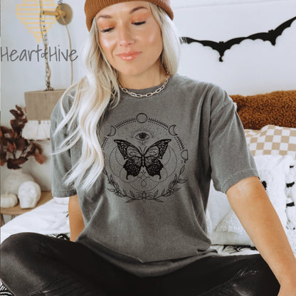 Pepper Comfort Colors tee with a black design of a butterfly, all-seeing eye, crescent moons, celestial symbols, and botanicals