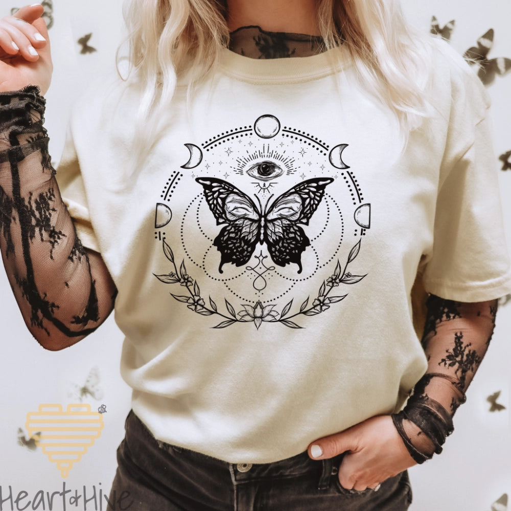 Ivory Comfort Colors tee with a black design of a butterfly, all-seeing eye, crescent moons, celestial symbols, and botanicals