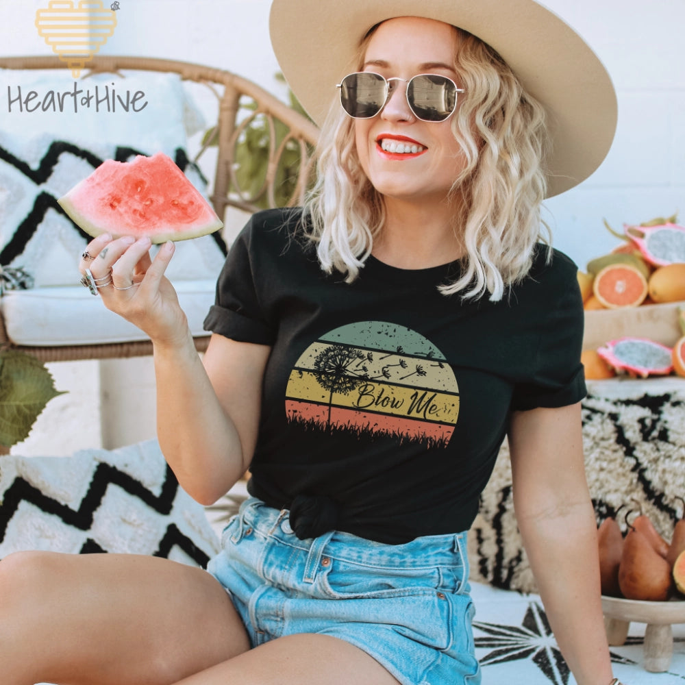 Black t-shirt with a retro sunset circle, grass, and the faded silhouette of a dandelion and 'Blow Me' text.