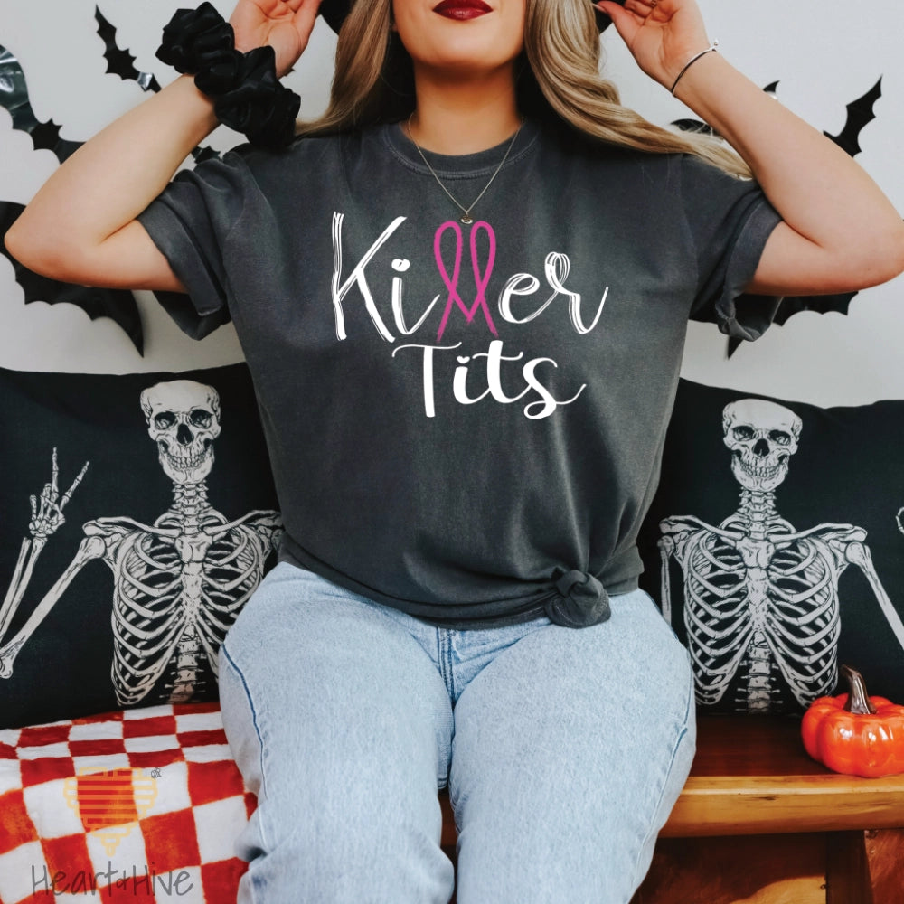 Pepper comfort colors tee featuring the phrase "Killer Tits" in black script, with the letter "ll" stylized as a pink breast cancer ribbon.